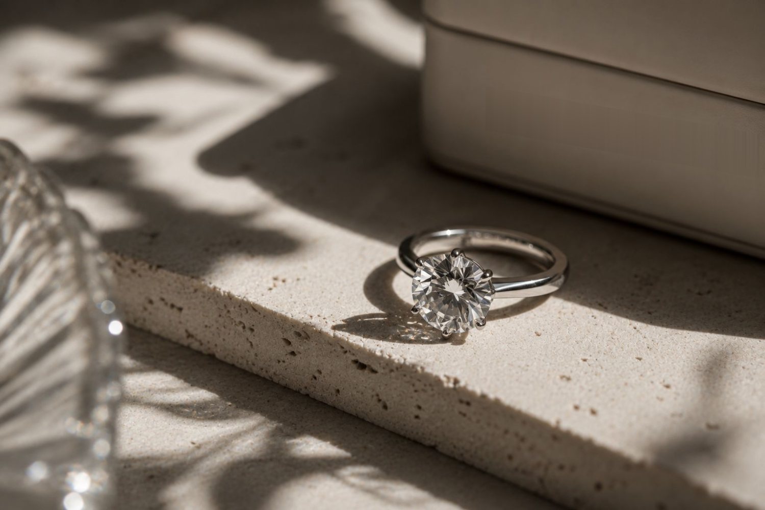 A round solitaire ring beside a cream presentation case in low sunlight